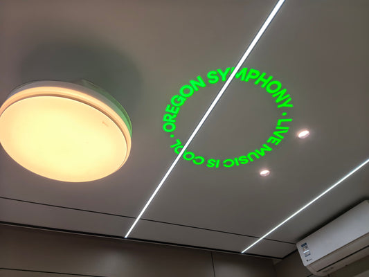 Green Oregon Symphony lettering projected onto a ceiling during a GoboUltra factory test, with no white background circle.